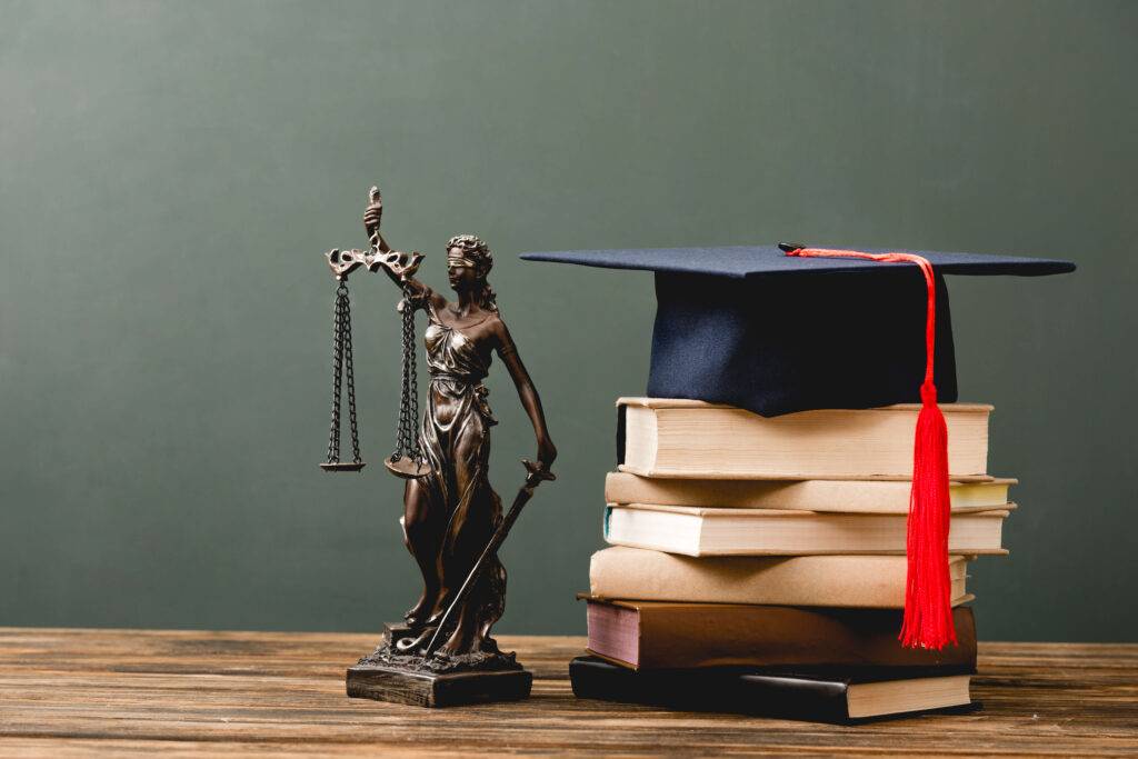 the law symbol statue next to a stack of books with a graduation cap on top of them all on a desk