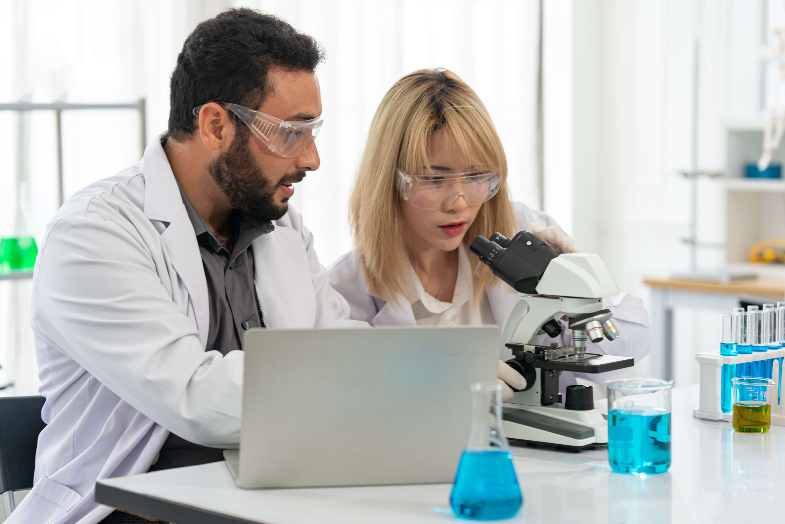 two scientists looking at microscope and laptop
